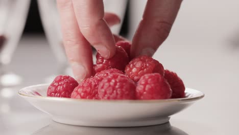 Detail-finger-grabbing-raspberry-pieces-from-a-plate-while-cooking-a-dessert-sweet-healthy-meal-close-up-shot