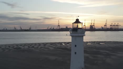Low-tide-aerial-view-coastal-lighthouse-sunrise-shipping-port-cranes-horizon-lantern-closeup-dolly-right