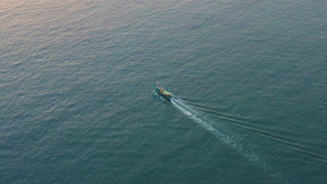 A-colorful-local-fishing-boat-traveling-through-the-tropical-waters-of-Bali-during-Sunset,-aerial-follow