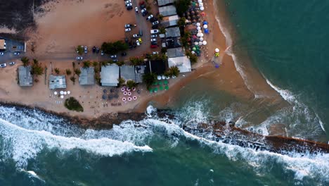 Beautiful-aerial-drone-top-bird'e-eye-view-of-waves-crashing-into-the-tropical-rocky-coast-with-beach-shops-and-umbrellas-in-the-town-of-Tibau-do-Sol-near-Pipa,-Brazil