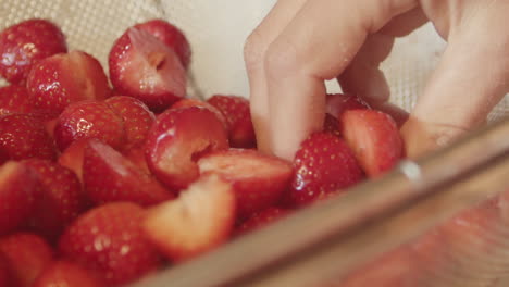 Fresh-sliced-strawberries-in-strainer-basket-as-hand-reaches-inside,-close-up