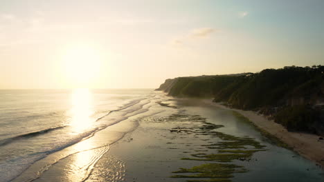 Low-golden-sun-reflecting-off-tropical-waters-off-of-Melasti-beach,-Bali,-aerial-dolly-slow-motion