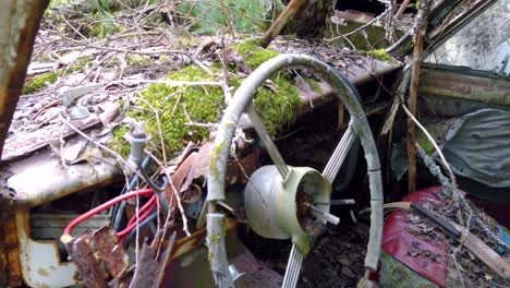Interior-of-old-abandoned-deteriorated-vehicle-with-broken-steering-wheel,-wires,-moss-growing-on-dashboard-and-falling-to-pieces,-close-up-pan