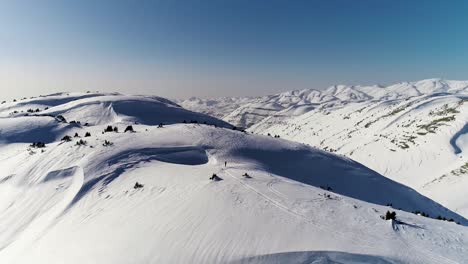 Sensational-flight-above-white-snow-covered-Akoura-mountain-ridge-towards-bright-blue-sky-and-range,-Lebanon,-overhead-aerial-approach
