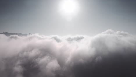 Rising-aerial-view-above-thick-cloud-cover,-with-sun-shining-above-clouds