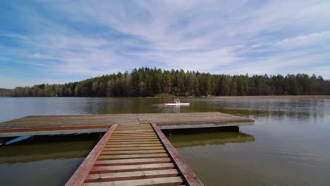 young-man-riding-a-pedal-boat-past-a-wooden-pier-on-a-pond-surrounded-by-a-wood
