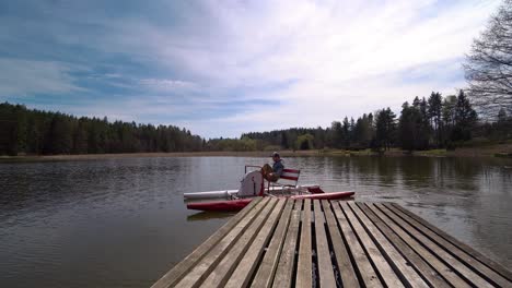 young-man-on-a-pedal-boat-leaving-a-wooden-pier-on-a-pond-surrounded-by-a-wood