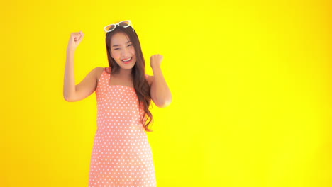 A-young-Asian-woman-in-a-sundress-and-sunglasses-expresses-her-positive-triumphant-emotions