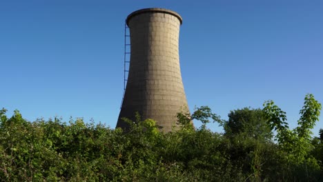 Tall-concrete-tower-of-coal-plant-station-covered-in-green-grass-and-thorns-on-abandoned-industrial-area