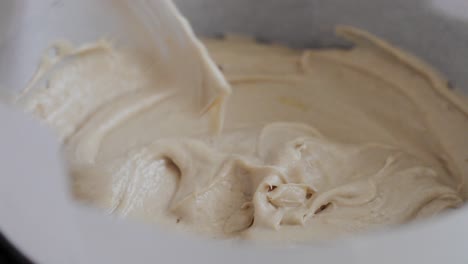 Chef-mix-cream-dough-in-a-metal-bowl-with-plastic-spoon-while-cooking-delicious-cake-at-local-kitchen-close-up