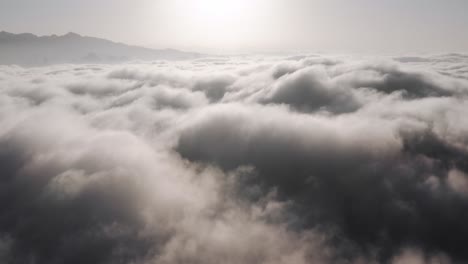 Aerial-view-above-thick-clouds-rolling-over-mountain-peaks