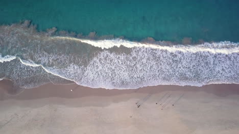 Top-Down-Aerial,-waves-breaking-on-the-sandy-shore-of-Shoal-Bay-in-Australia,-people-walking-on-beach-during-golden-hour