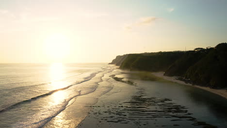 Golden-sunlight-reflects-off-warm-tropical-water,-waves-crashing-on-Melasti-beach,-South-Bali,-aerial-hyperlapse
