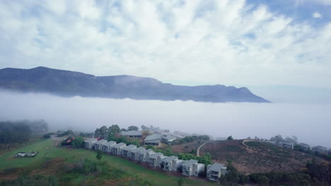 Early-morning-fog-covers-Hunter-Valley-with-a-resort-on-top-of-hill,-aerial