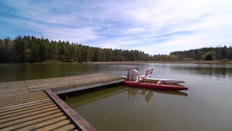 pedal-boat-parked-at-a-wooden-pier-on-a-pond-surrounded-by-a-forest