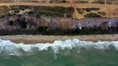 Gorgeous-aerial-drone-left-trucking-shot-of-a-large-cliff-dropping-straight-to-the-beach-and-ocean-at-the-tropical-Sun-beach-near-Joao-Pessoa,-Brazil-on-a-warm-summer-evening