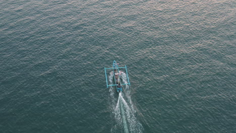 Tracking-above-and-behind-a-local-tour-boat-as-it-motors-across-open-water-off-the-coast-of-Bali,-aerial
