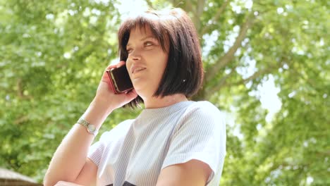 Attractive-good-looking-female-with-black-hair-bob-haircut-speaking-on-the-phone-out-in-the-forest
