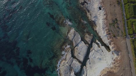 Aerial-view,-looking-down-on-the-sea-caves-on-the-coast-with-clear-blue-waters-lapping-the-shoreline