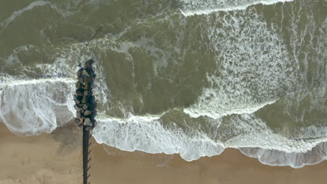 Aerial-shot-of-the-might-sea-and-its-waves-crashing-on-a-deserted,-golden-sand-beach