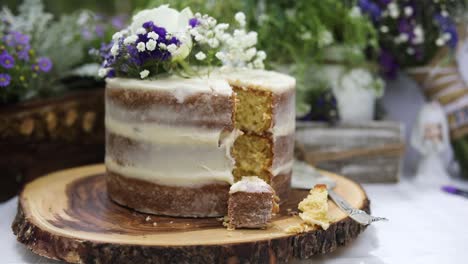 Delicious-eaten-piece-of-decorative-white-icing-wedding-cake-with-flowers-on-top-on-celebratory-day,-close-up-pull-back