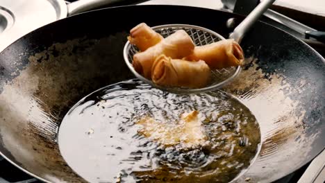 Hot-Asian-spring-rolls-are-finished-frying-in-steel-wok-and-removed-with-slotted-metal-mesh-scoop,-close-up-static