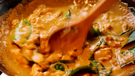 Delicious-Thai-food-meal-of-Chicken-and-vegetables-and-red-curry-are-cooking-and-stirred-in-black-wok-with-slatted-wooden-spoon,-static-close-up