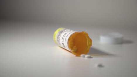 Weiße-Pillen,-Die-Aus-Einer-Umgestürzten-Gelben-Tablettenflasche-Auf-Einem-Weißen-Tisch-Verschüttet-Werden