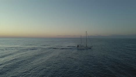 Idyllic-luxury-sailing-ship-cruising-calm-peaceful-blue-sea-ocean-seascape-at-sunrise-aerial-pull-back