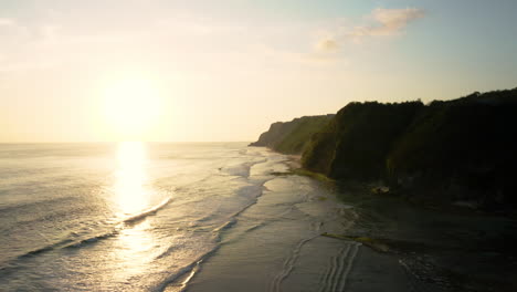 Golden-sunlight-reflects-off-warm-tropical-water,-waves-crashing-on-Melasti-beach,-South-Bali,-aerial