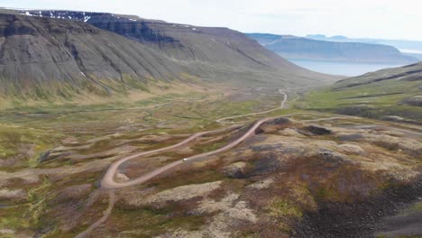 Areal-shot-of-white-car-going-uphill-across-gravel-roads-in-beautiful-nature-of-Iceland