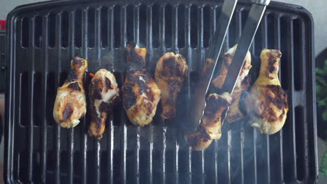 Top-down-view-of-charred-chicken-being-flipped-with-tongs-on-barbecue-grill