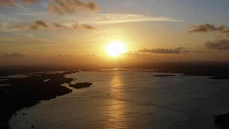 Atemberaubende-Breite-Luftdrohnenaufnahme-Eines-Goldenen-Sonnenuntergangs,-Der-Sich-An-Einem-Warmen-Sommerabend-Auf-Einem-Riesigen-Amazonischen-Fluss-In-Der-Tropischen-Strandstadt-Tibau-Do-Sol-In-Der-Nähe-Von-Pipa-Im-Norden-Brasiliens-Widerspiegelt