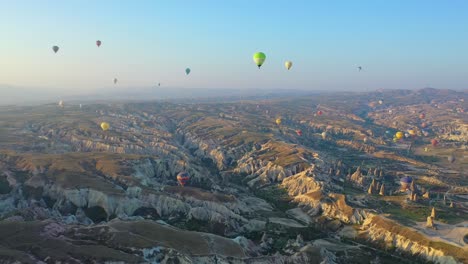 Many-hot-air-balloons-floating-above-Cappadocia-landscape,-panoramic-forward-aerial