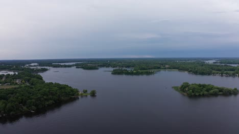 Wide-descending-aerial-shot-of-a-Midwestern-lake-as-the-sky-and-water-darkens-from-an-impending-storm