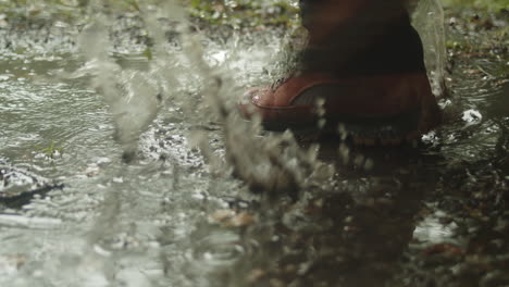 Hiker-splashes-through-puddle-in-rain,-close-up,-slow-motion