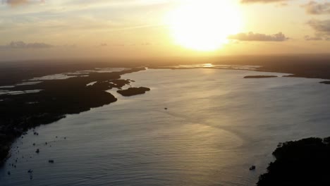 Stunning-aerial-drone-left-trucking-shot-of-a-golden-sunset-reflecting-onto-a-giant-amazonian-river-in-the-tropical-beach-town-of-Tibau-do-Sol-near-Pipa-in-Northern-Brazil-on-a-warm-summer-evening