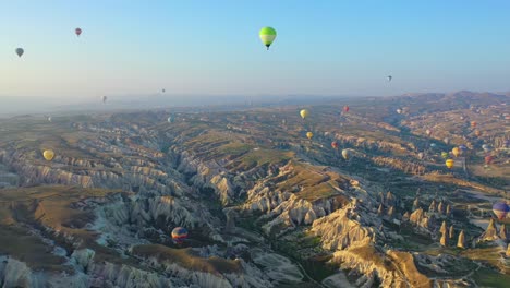 Many-hot-air-balloons-floating-above-Cappadocia-landscape,-panoramic-backwards-aerial