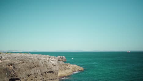 Peaceful-ocean-shore-view-with-rock-cliff,-crashing-waves-and-blue-sky-at-Cascais-Portugal-4K-jib-shot