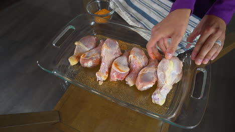 Seasoning-raw-chicken-drumsticks-with-orange-spice-in-glass-baking-pan