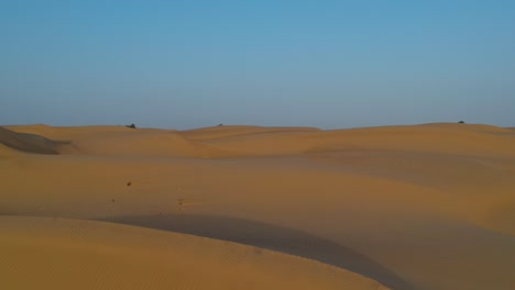 Drone-flying-through-the-desert-while-sand-dunes-are-moving-towards-the-viewer-whith-blue-sky-in-the-background-at-Wahiba-Sands-in-Oman