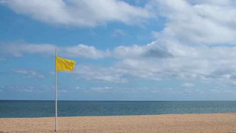 Bandera-De-Advertencia-Amarilla-Que-Sopla-En-El-Viento-En-Un-Día-Soleado-En-La-Playa-Vacía