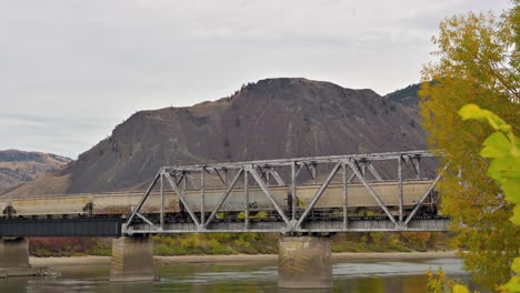 a-container-Train-crossing-the-South-Thompson-River-via-the-CNR-Bridge-close-to-Riverside-Park-East-of-Downtown-Kamloops-on-an-overcast-day-in-autumn