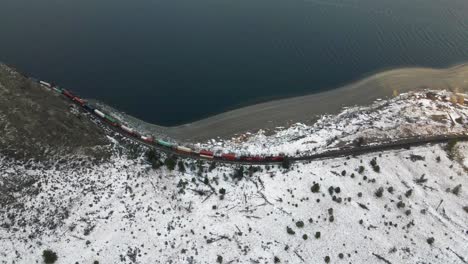 Overhead-shot-of-a-train-driving-along-Kamloops-Lake-in-the-winter,-showing-a-partially-snow-covered-desert-landscape-in-British-Columbia's,-Nicola-Thompson-Region