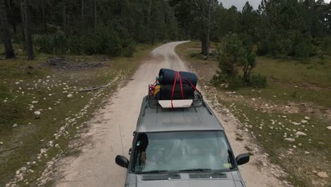 Vista-Frontal-De-Un-Jeep-Con-Portaequipajes-Conduciendo-Por-Una-Carretera-De-Montaña-En-El-Bosque,-Viaje-En-Coche-A-La-Cima-De-La-Montaña,-Aéreo