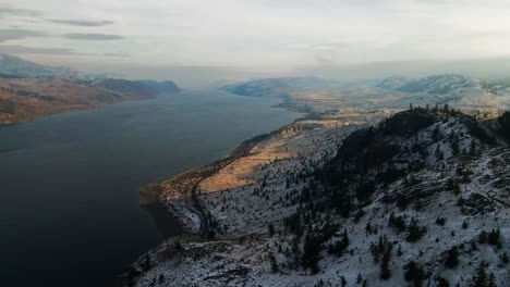 Panoramic-Aerial-Shot-of-Kamloops-Lake-during-winter,-a-partially-snow-covered-hilly-desert-landscape-beautifully-lit-during-golden-hour-with-large-shaded