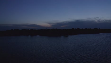 Aerial-reverse-shot-with-boat-on-lake-passing-by-during-twilight