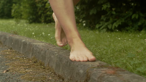 Female-bare-feet-walk-along-street-curb,-slow-motion,-low-angle