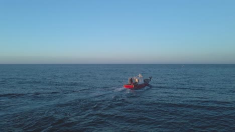 Small-fishing-boat-on-the-open-water-near-Playa-del-Cura,-Spain-in-the-evening-against-a-clear-blue-sky--aerial-low-angle