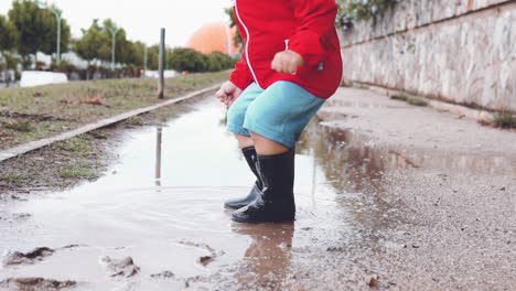 Kid-wearing-rubber-boots-jumping-in-a-muddy-puddle-and-splashing-water-in-slow-motion